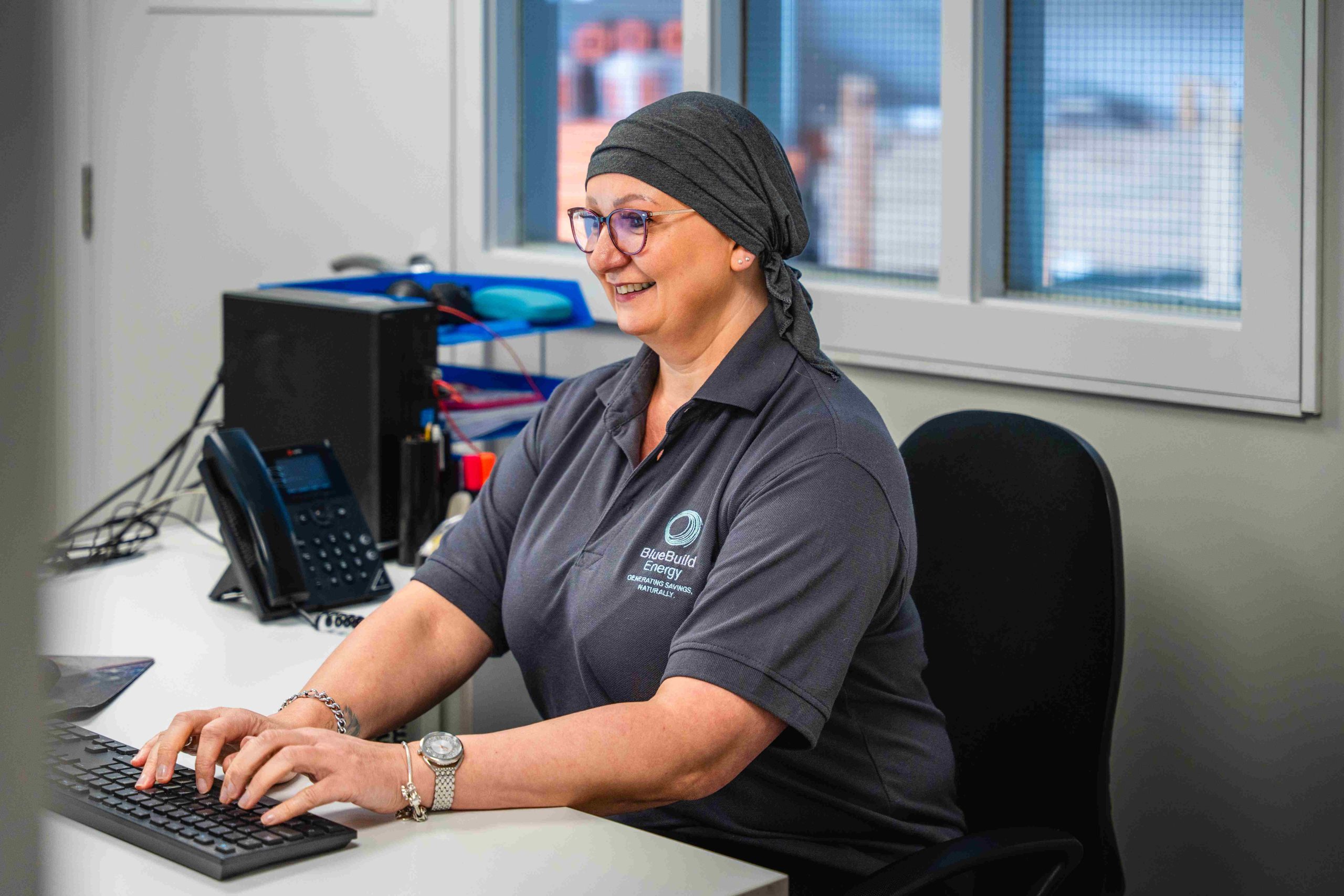 A smiling BlueBuild Energy staff member working at an office desk computer.